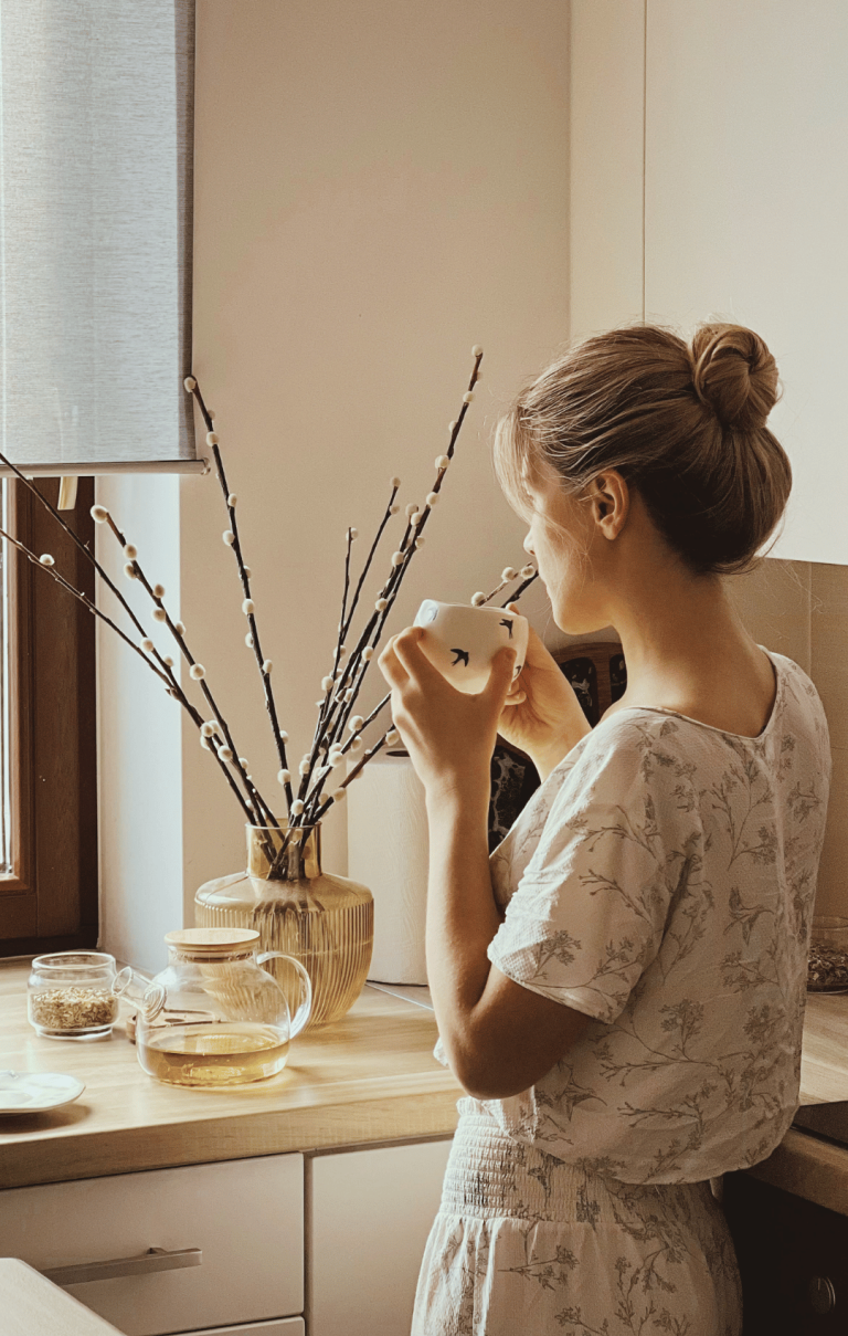 woman looking out the window holding a cup of tea